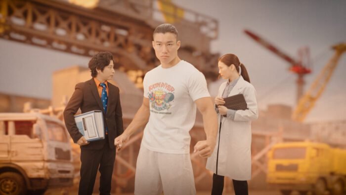 a scientist and a businessman argue in front of a burning construction site, a large body builder standing in the foreground between them. (Hot Spring Shark Attack)
