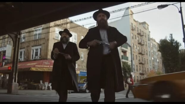 The two Jewish mobsters, Lipa and Shmully Drucker (Liev Schreiber & Vincent D'Onofrio) walk forward down the street while equipping their guns.