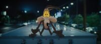 Wile E. Coyote gives a worried look while crouched on top of a moving semi truck in the film, “Coyote vs. Acme” (2026).