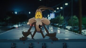 Wile E. Coyote gives a worried look while crouched on top of a moving semi truck in the film, “Coyote vs. Acme” (2026).