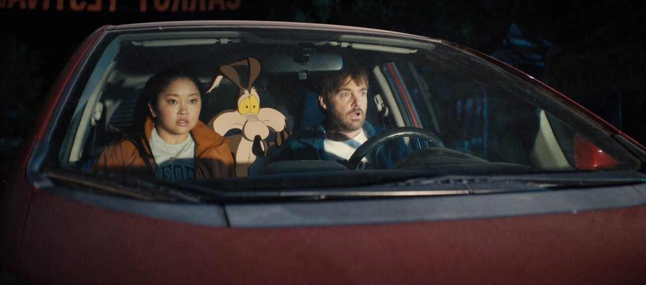 Paige Avery (Lana Condor), Wile E. Coyote, and Kevin Avery (Will Forte), in a car, look on in shock as light illuminates their faces in the film, “Coyote vs. Acme” (2026).