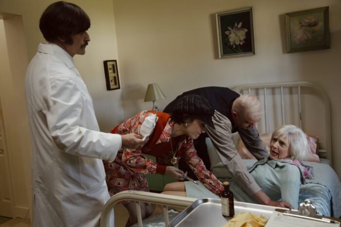 A hospital scene with a man and a woman restraining a woman in bed while her doctor looks on.