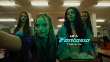 A young woman with braids and butterfly clips outstretches her arm past the camera while three other girls stand behind her, one holding a lunch tray.