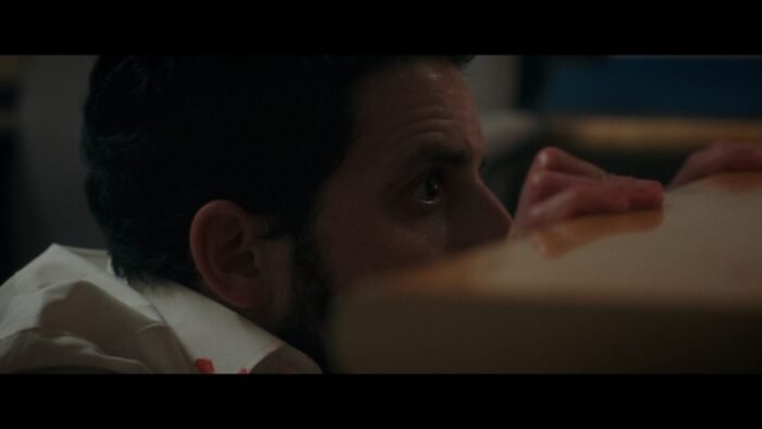 A man cowers behind a desk, peeking out slightly.