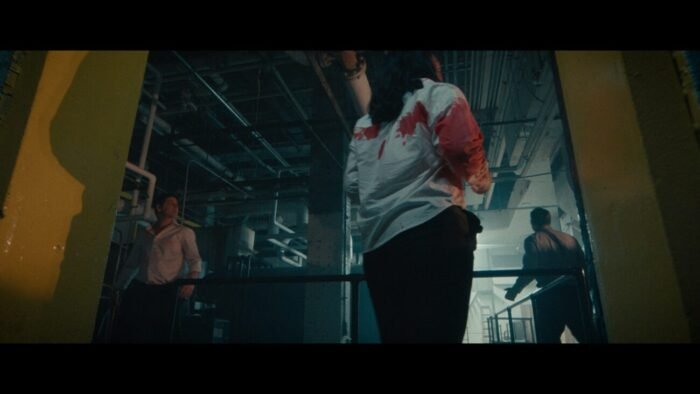 A trio of individuals covered in blood search for a way out from a pipe filled room.