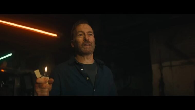 Hutch (Bob Odenkirk) stands with a lighter in his hand.