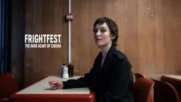 A woman with her makeup running down her cheeks sits at an old restaurant table against a wall with wood paneling (Odyssey, 2025)