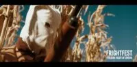 A hooded figure holds up a shotgun in a cornfield (The Rows)
