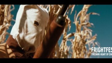 A hooded figure holds up a shotgun in a cornfield (The Rows)