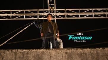 A stunt performer at the edge of a building rigged to a crossbeam behind him.
