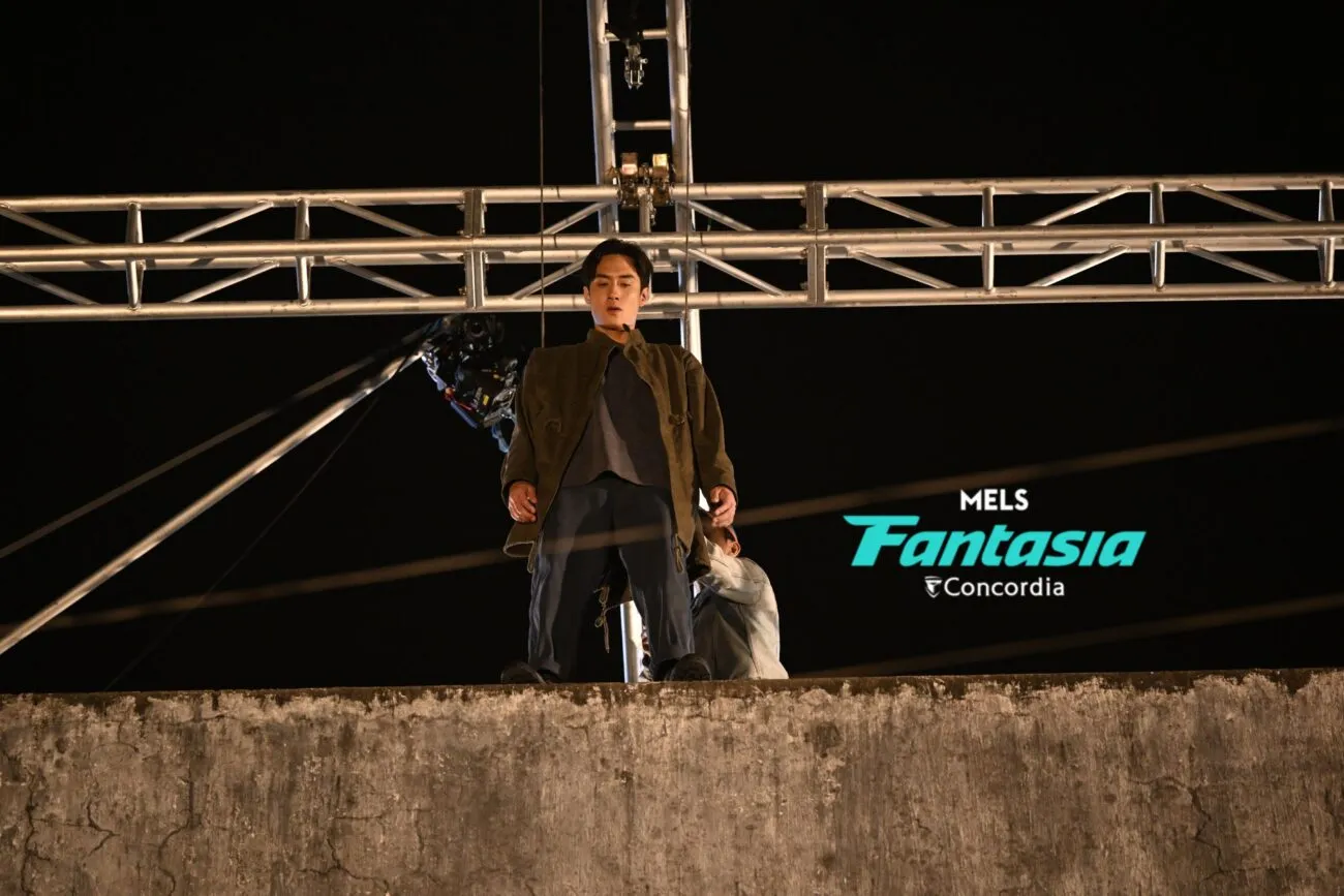 A stunt performer at the edge of a building rigged to a crossbeam behind him.