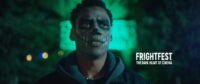 A man with his face painted like a skeleton stands in front of a green background. (The Haunted Forest)