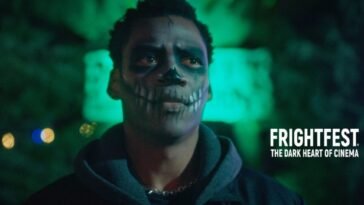 A man with his face painted like a skeleton stands in front of a green background. (The Haunted Forest)