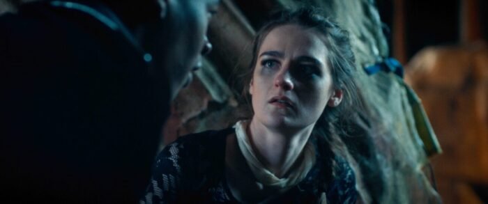 A young woman looks concerned as someone speaks to her in the foreground.