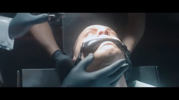 Max is held by a strap on the mouth, and is being prepared for some type of surgery (The Home)
