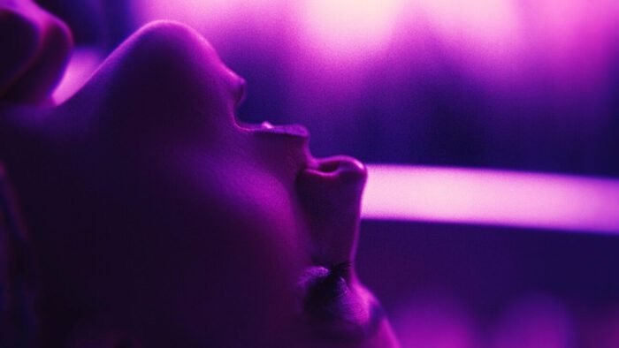 A woman with her back and eyes shut under purple lighting (Touch Me)