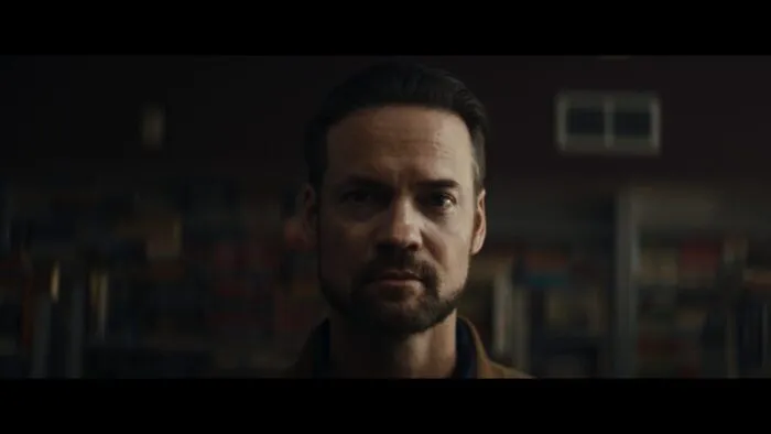 An earnest looking man with a beard looks into the camera