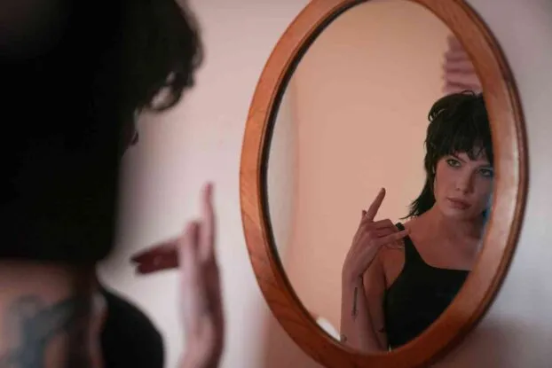 Mandy (Halsey) looks at her reflection in an oval mirror. She's wearing a black dress