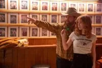 Lefty (Paul Walter Hauser) stands behind Penny Jo (Sydney Sweeney) teaching her how to throw a dart.