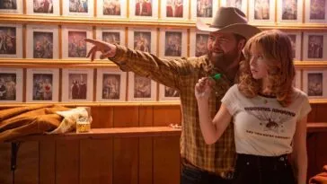 Lefty (Paul Walter Hauser) stands behind Penny Jo (Sydney Sweeney) teaching her how to throw a dart.