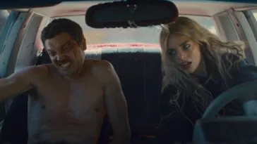 John is seen naked in the passenger seat while Edie is seen driving a car, both are leaning to their right as the car turns. (Eeenie Meanie)