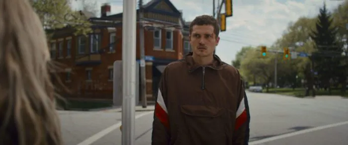 A man with a bloody face stands in a track suit at an intersection.