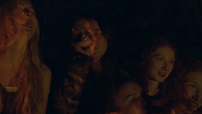 a hazy scene of on woman drinking from a bottle in the center and others laughing and smiling around her.