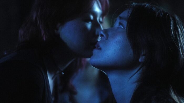 two women's faces are very close together one appearing confident, the other threatening, under the dark light of the moon