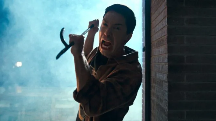 A man with an intense face, screams as he approaches the camera with a firepoker.