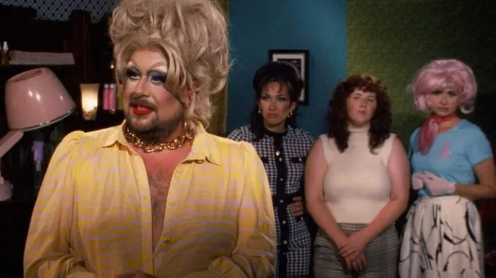 a drag queen stands in front of a trio of women