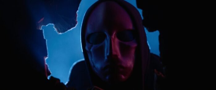 The Red Mask peers through a whole in the wall.