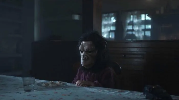 A child sits at a dinner table wearing a monkey mask.