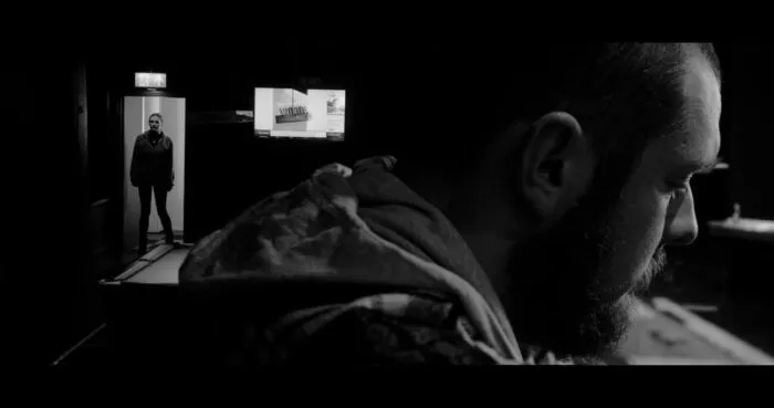 A close up of a man siting at a bar with another person standing in a doorway further away.