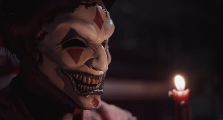 The jester's mask is lit by a candle.