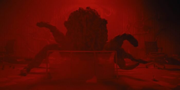 A tentacle monster rises out of some sort of a container beneath it in a red room (Kombucha)
