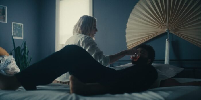 A man laying in bed is consoled by a woman stroking his face at his bedside.