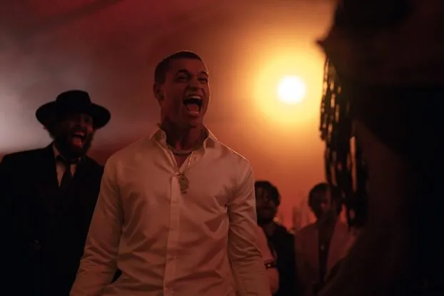 Cam (Tyriq Withers) stands in a crowd with a light behind him, yelling.