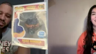 Steven Ray Byrd, wearing a Looney Tunes T-shirt, holds up Wile E. Coyote and Road Runner Funko Pops in autographed boxes while talking to Jamie Lee, wearing an orange Looney Tunes hoodie featuring Wile E. Coyote and Road Runner, a Daffy Duck key chain tied to one string on the hoodie.