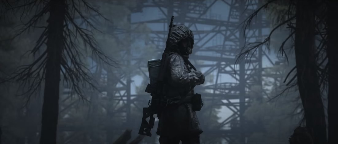 A man in a long coat and gasmask with a rifle over his shoulder walks through a dark forrest. He turns and looks at the camera