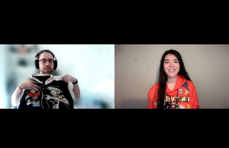 Alexis Bonhomme holds up a black and white bomber jacket featuring the Road Runner and Wile E. Coyote while talking to Jamie Lee, wearing an orange Looney Tunes hoodie featuring Wile E. Coyote and Road Runner, a Daffy Duck key chain tied to one string on the hoodie.