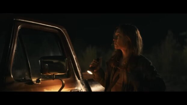Mia (Camille Sullivan) stands next to her vehicle with a flashlight in hand.