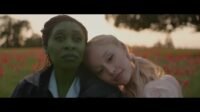 Elphaba (Cynthia Erivo) and Glinda (Ariana Grande). Glinda is leaning her head on Elphaba's shoulder. There is a tree in the background.