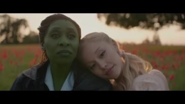 Elphaba (Cynthia Erivo) and Glinda (Ariana Grande). Glinda is leaning her head on Elphaba's shoulder. There is a tree in the background.