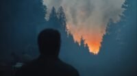 Shadow of a man facing away and looking at the woods, with a orange glow from a fire in the distance