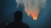 Shadow of a man facing away and looking at the woods, with a orange glow from a fire in the distance