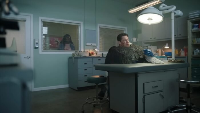 Eagly, an eagle, hugs Peacemaker in a hospital, with Leota Adebayo watching behind a window in the background.