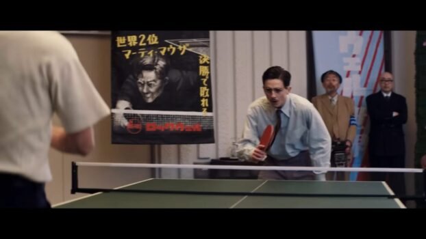 Marty prepares for one final game. He's standing behind one side of the ping pong table.