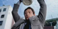 Yoo Man-soo (Lee Byung Hun) holds a plant pot aloft in a threatening manner in No Other Choice